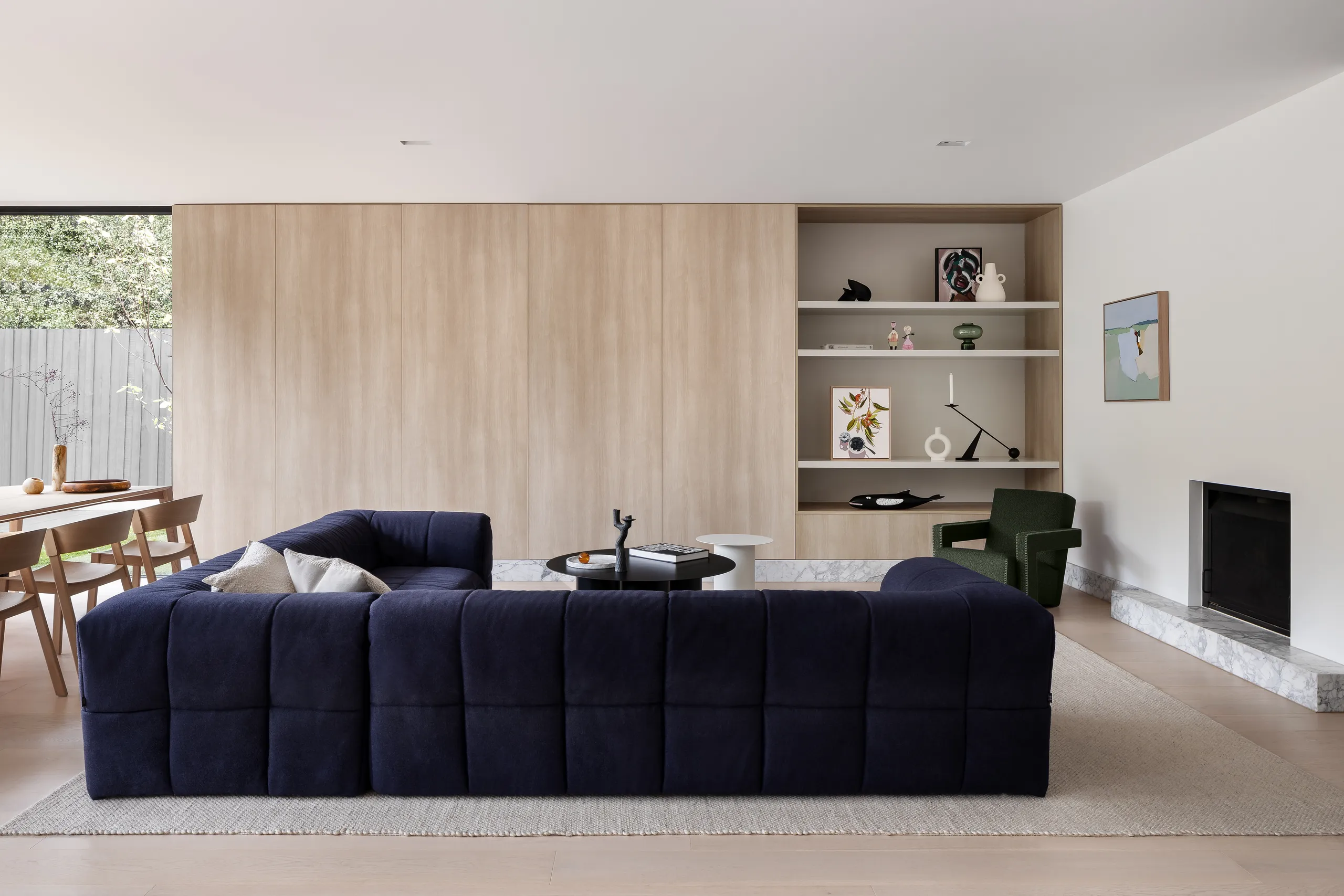 Living room with a navy modular sofa, full-height timber joinery and open shelving, dining beyond