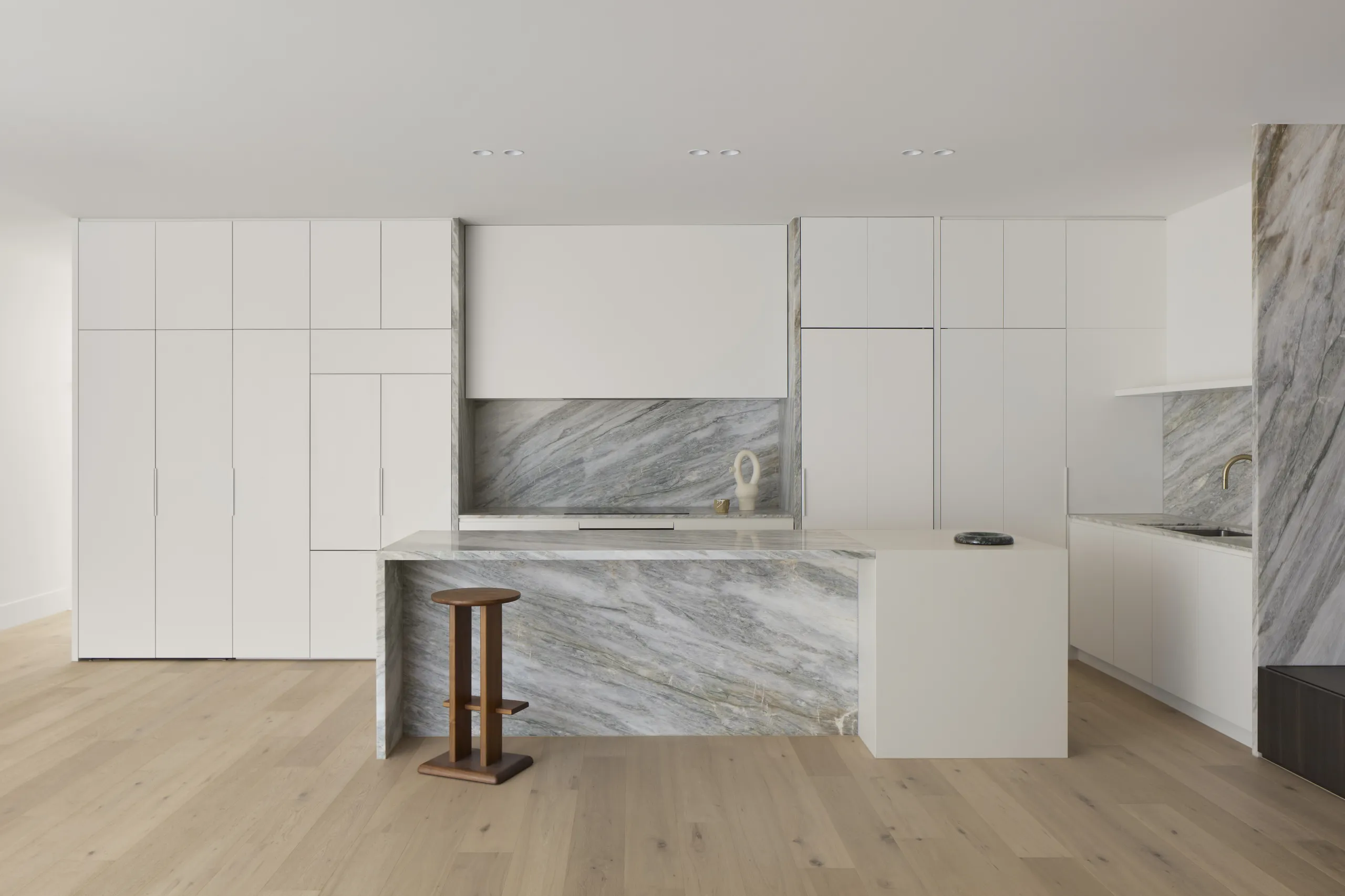 White kitchen joinery with a marble-topped island and a small timber stool