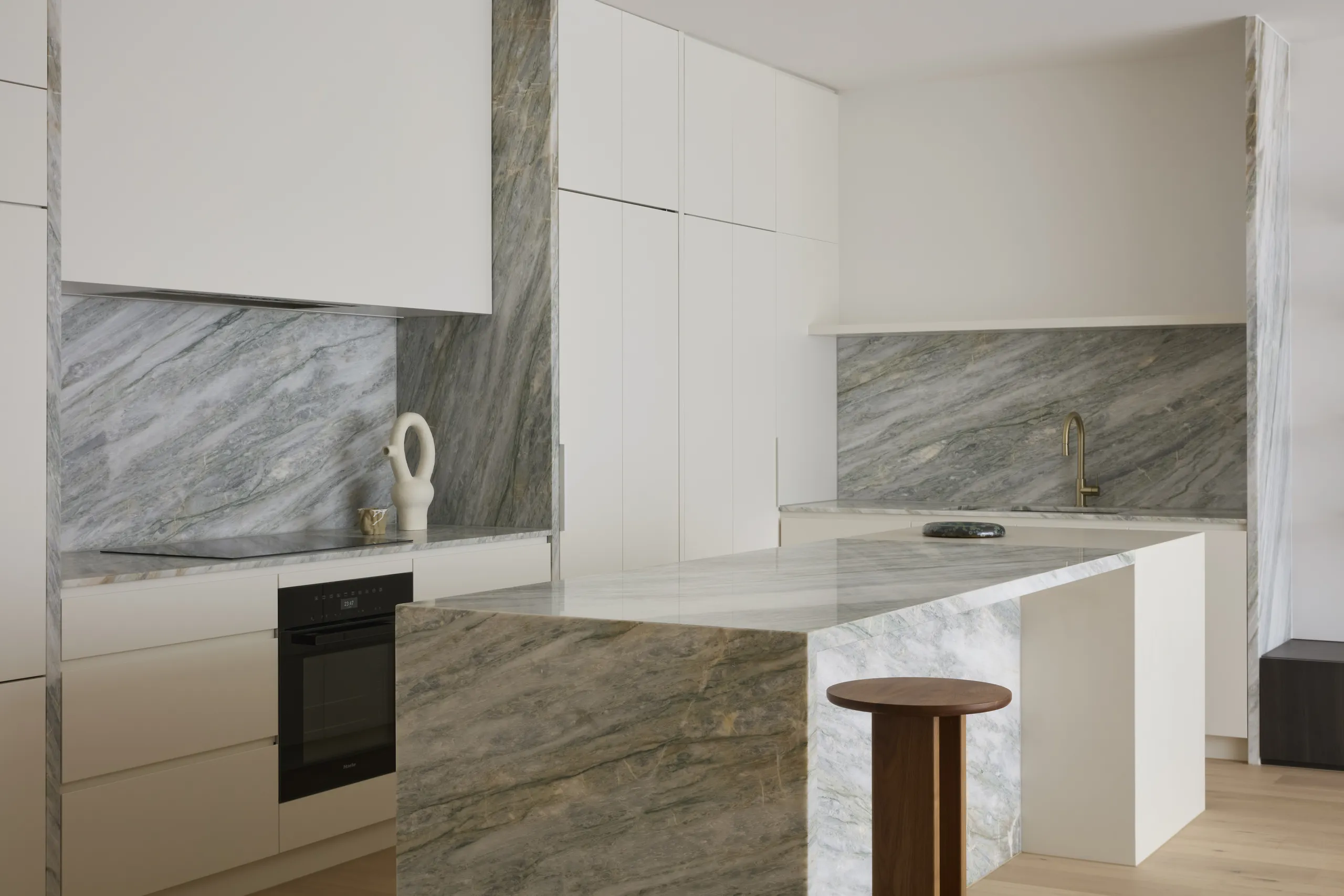 Kitchen with a grey-veined marble island and splashback set against white joinery