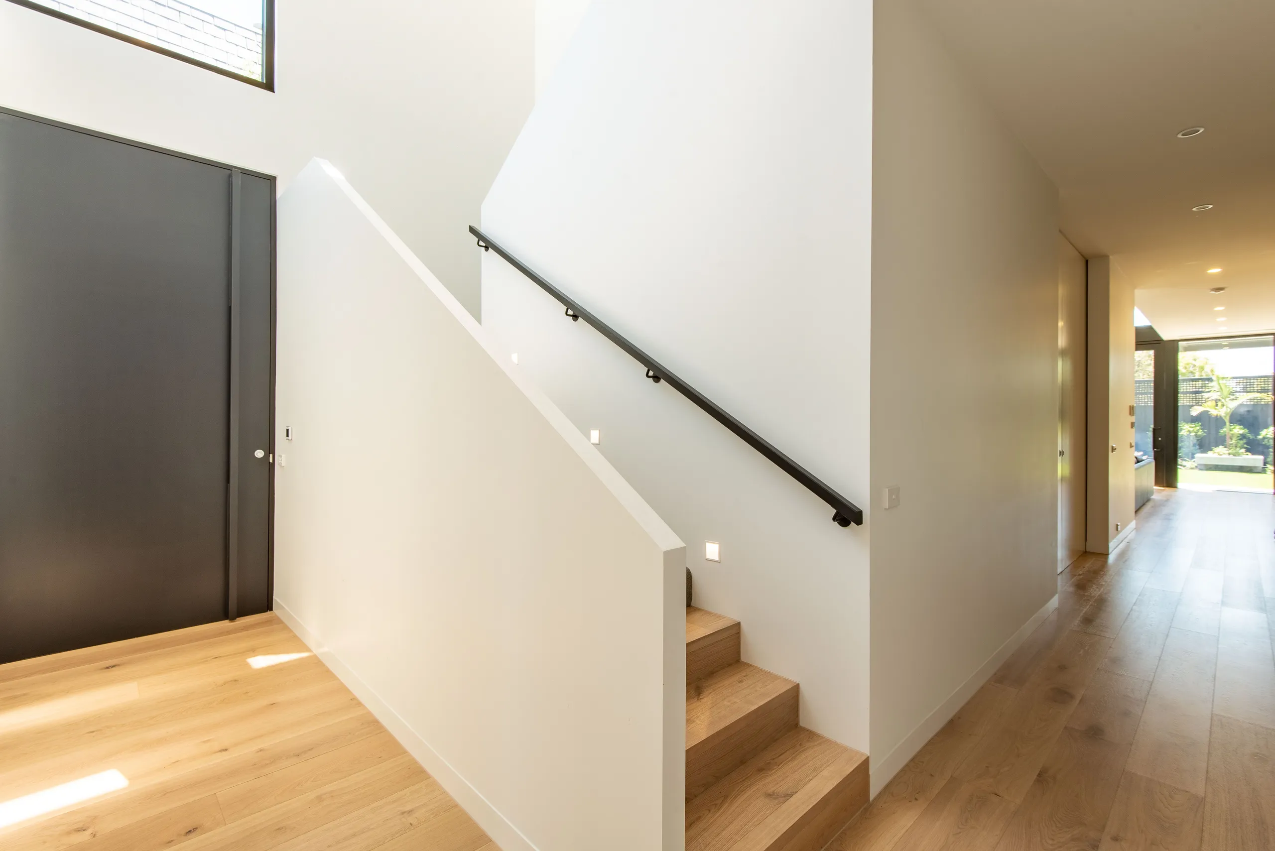 Timber stair rising beside a white wall towards a garden outlook