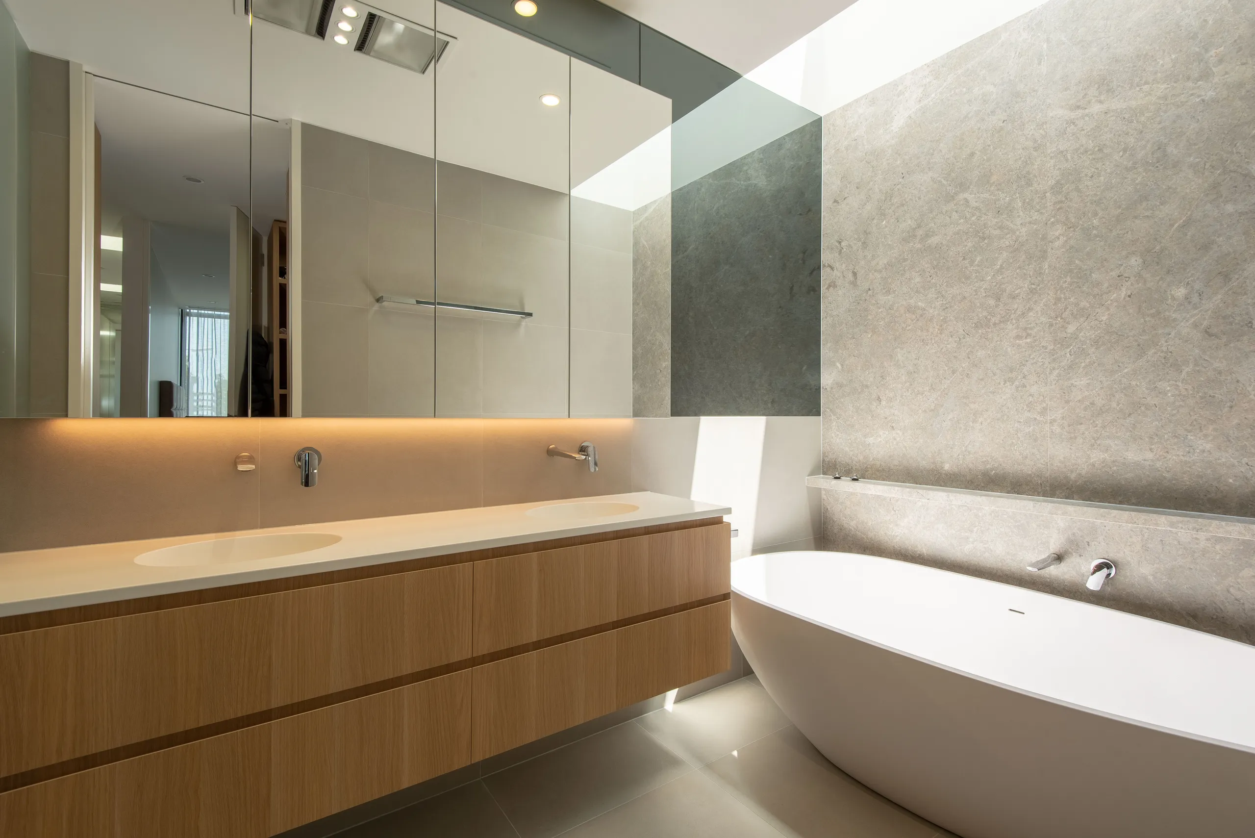Vanity run in timber and stone with a mirrored wall and a freestanding bath