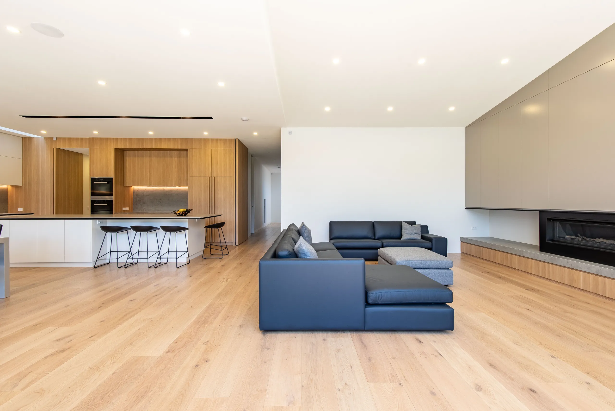 Open plan living and kitchen with pale timber floors and a linear fireplace